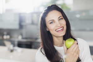 smiling woman in kitchen holding an apple